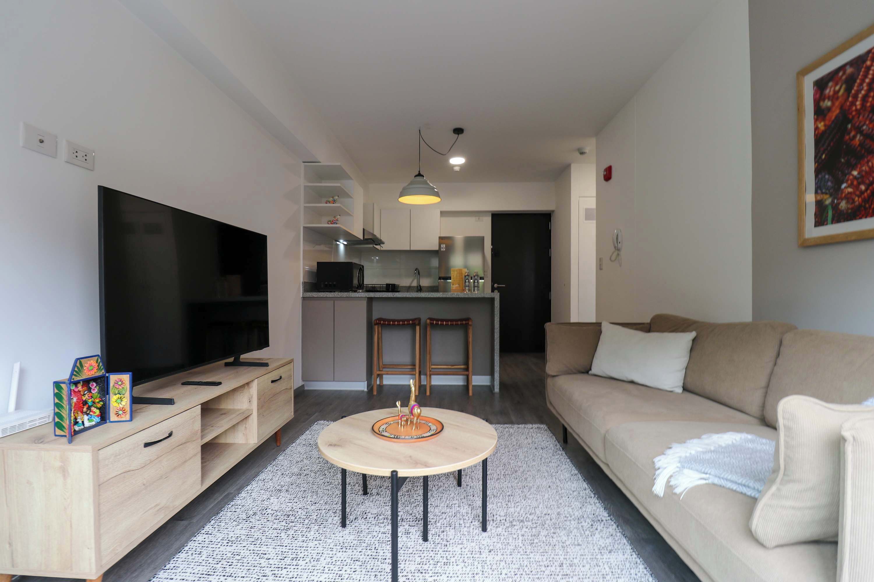 A modern living room with a flat-screen TV, wooden entertainment unit, round coffee table, and a beige sofa.