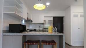 A modern kitchen with a microwave, stove, and refrigerator. There are two stools under the counter and a hanging light fixture. - w* | Bright 1BR in Historic Cusco w/ Balcony (Cusco)