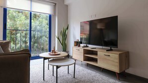 A modern living room with a large TV, a wooden cabinet, a round table, and a balcony with blue railings. - w* | Bright 1BR in Historic Cusco w/ Balcony (Cusco)
