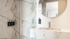 A bathroom with a marble wall, a round mirror, a white sink, and a glass shower enclosure. - w *|Grand 2BR w/ Lovely Terrace in Bocagrande (Cartagena de Indias)