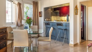 A modern kitchen with a bar area, a dining table with chairs, and a view of the outside through large windows. - Panoramic Views from the 17th, by Veeve (Paris)