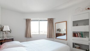 A hotel room with a large bed, a bedside table with a lamp, a mirror, and a bookshelf. - Panoramic Views from the 17th, by Veeve (Paris)