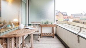 Ein Balkon mit Holztisch und -stühlen, einem Blumentopf und Blick auf die Nachbarschaft.