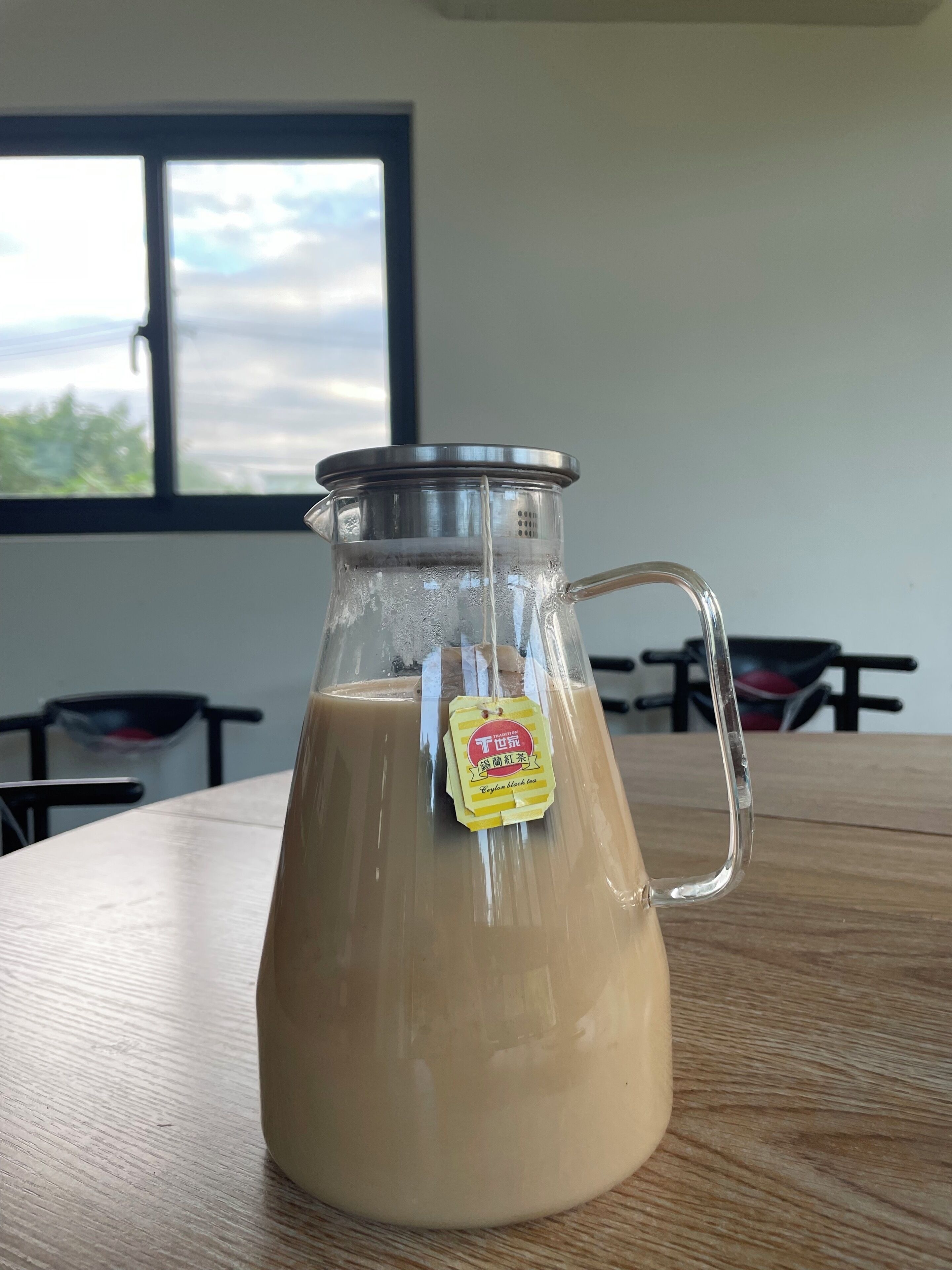 Un jarro de vidrio con té helado, una tapa de metal y un asa, sobre una mesa de madera.
