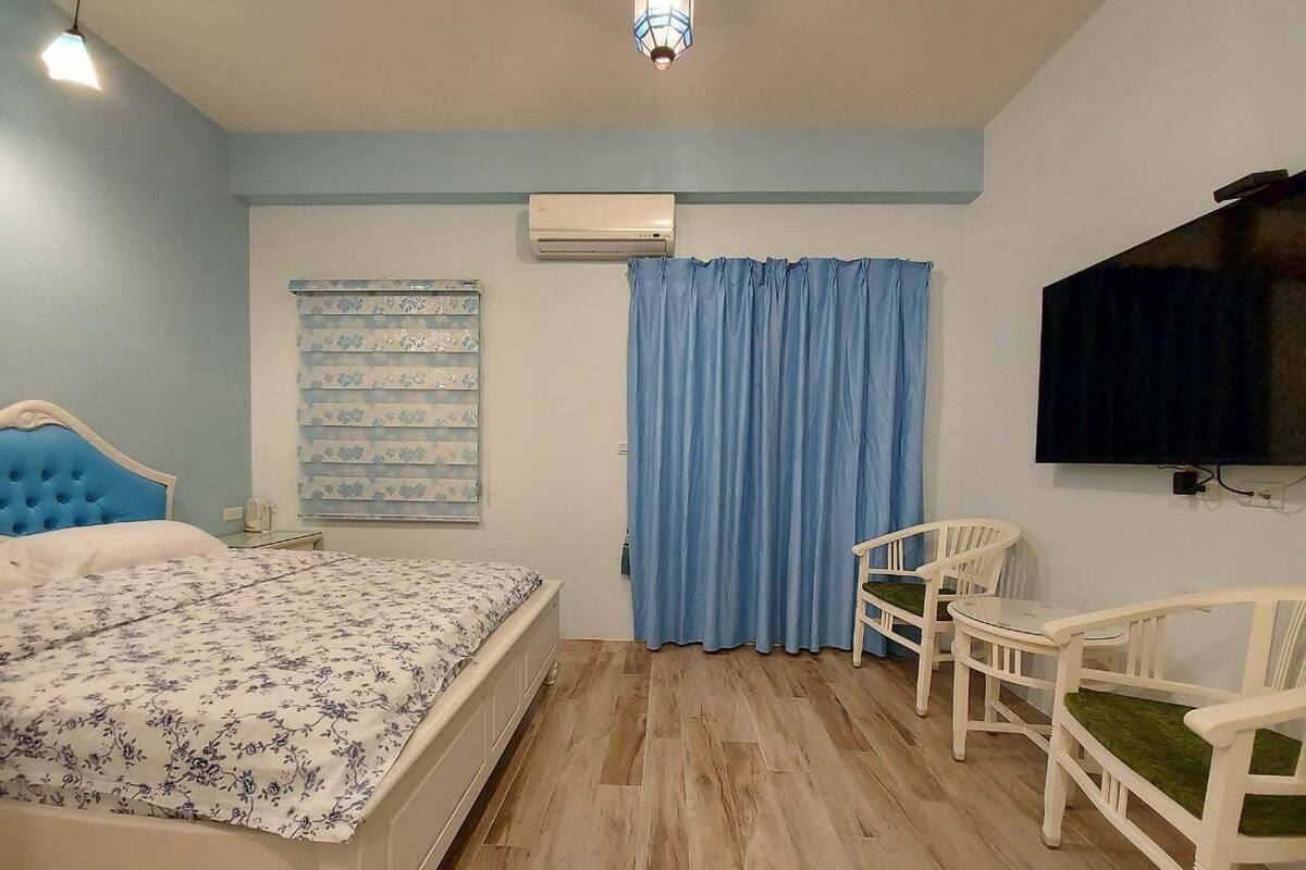 A bedroom with a bed, a TV, a window with curtains, and a small table with chairs.