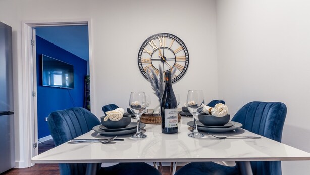 A dining table set with plates, bowls, wine glasses, and a bottle of wine, surrounded by blue chairs. - Durham Deluxe Apartment With Stunning Views (Durham)