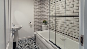 A bathroom with a white sink, a toilet, a bathtub, and a shower with a glass door. The floor has a black and white patterned tile. - Durham Deluxe Apartment With Stunning Views (Durham)