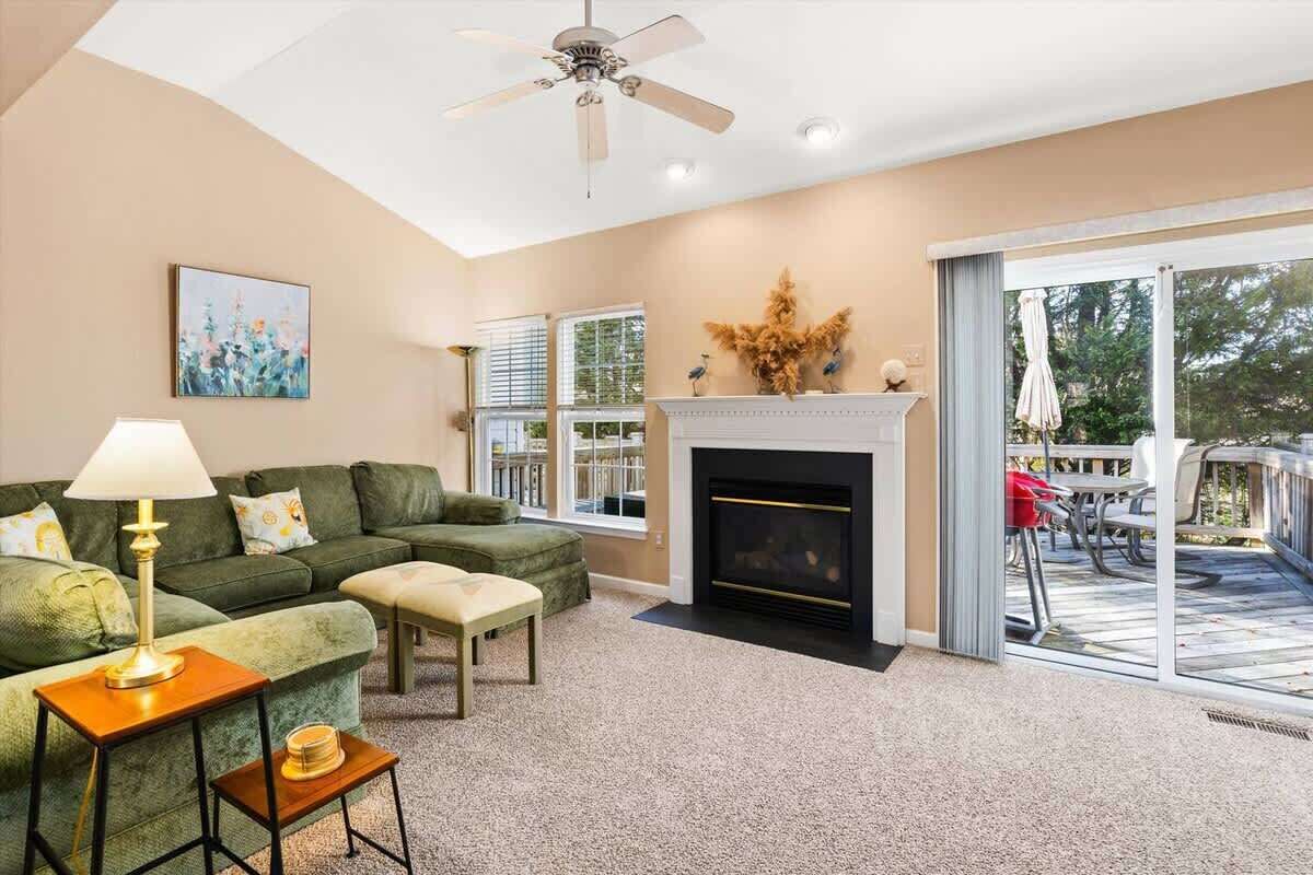 A living room with a green sofa, a small table with a lamp, a fireplace, and a view of the outdoors through large sliding glass doors.