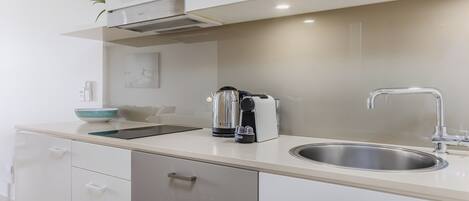 A modern kitchen with white cabinets, a stainless steel sink, a kettle, and a toaster.