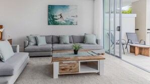A modern living room with a grey sofa, a wooden coffee table, and a large window with a view of the outdoors.