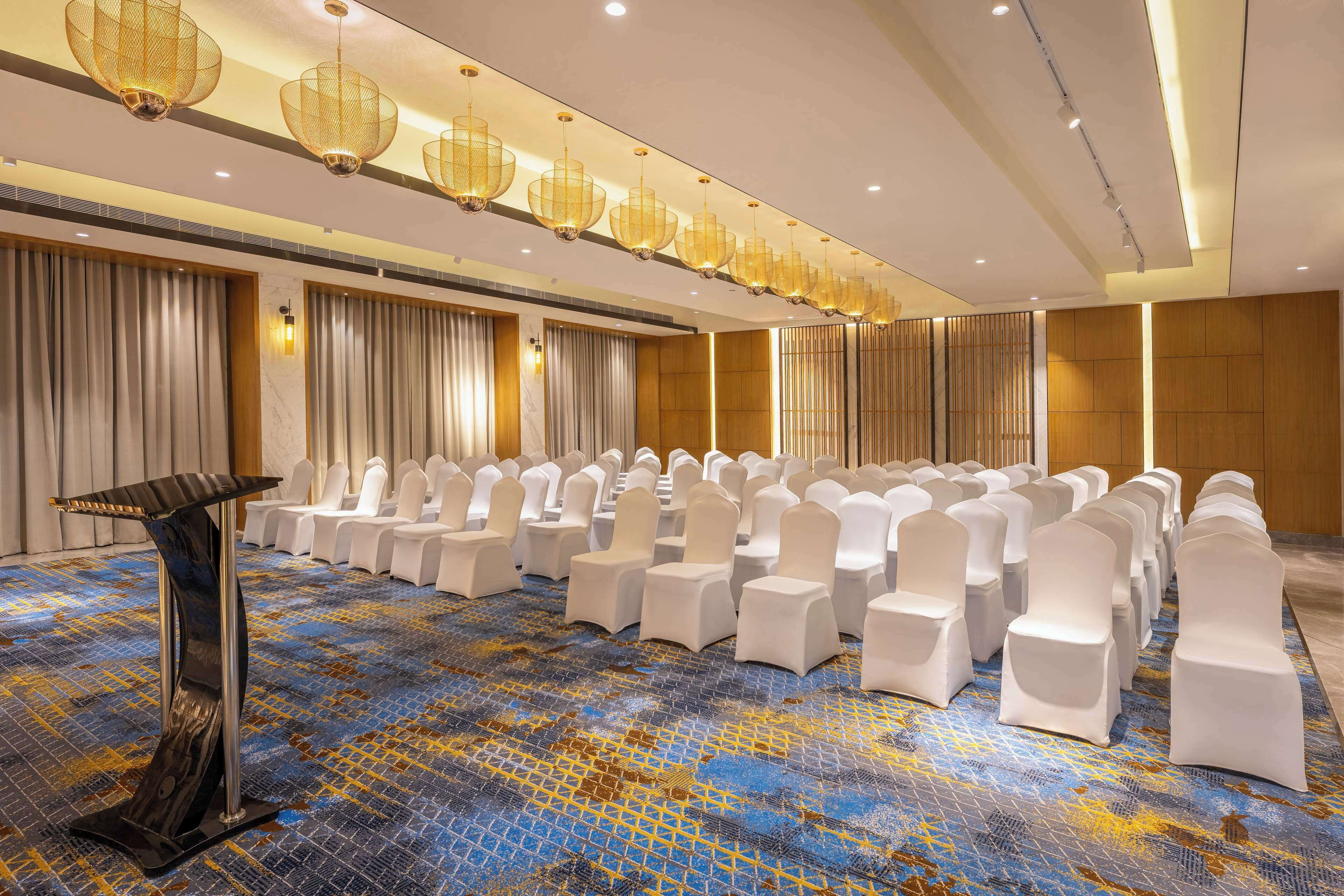 Una sala conferenze con file di sedie bianche, un leggio e una moquette fantasia.