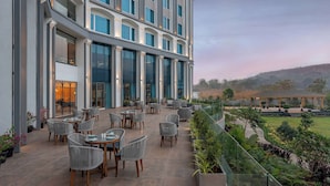 Un hotel moderno con un'ampia terrazza esterna, ampie finestre e vista su un giardino curato.