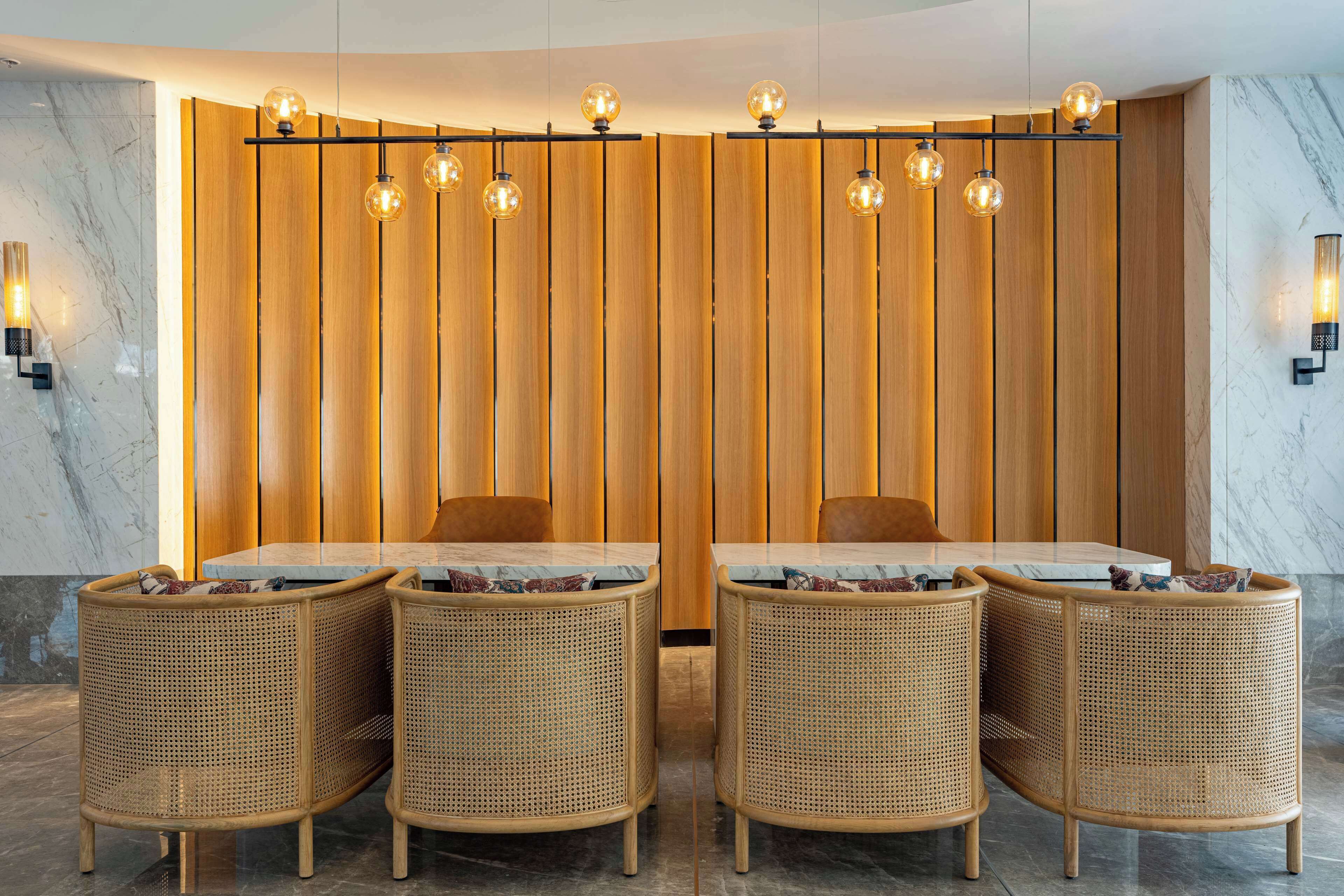 A dining area with a wooden partition, four wicker chairs, a marble table, and hanging spherical light fixtures.