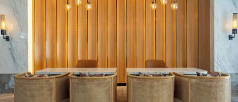 A dining area with a wooden partition, four wicker chairs, a marble table, and hanging spherical light fixtures.