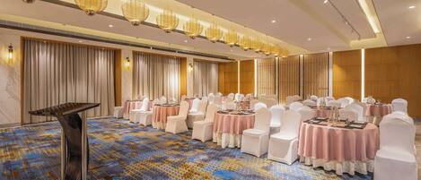 A banquet hall with round tables, white chairs, and a patterned carpet.