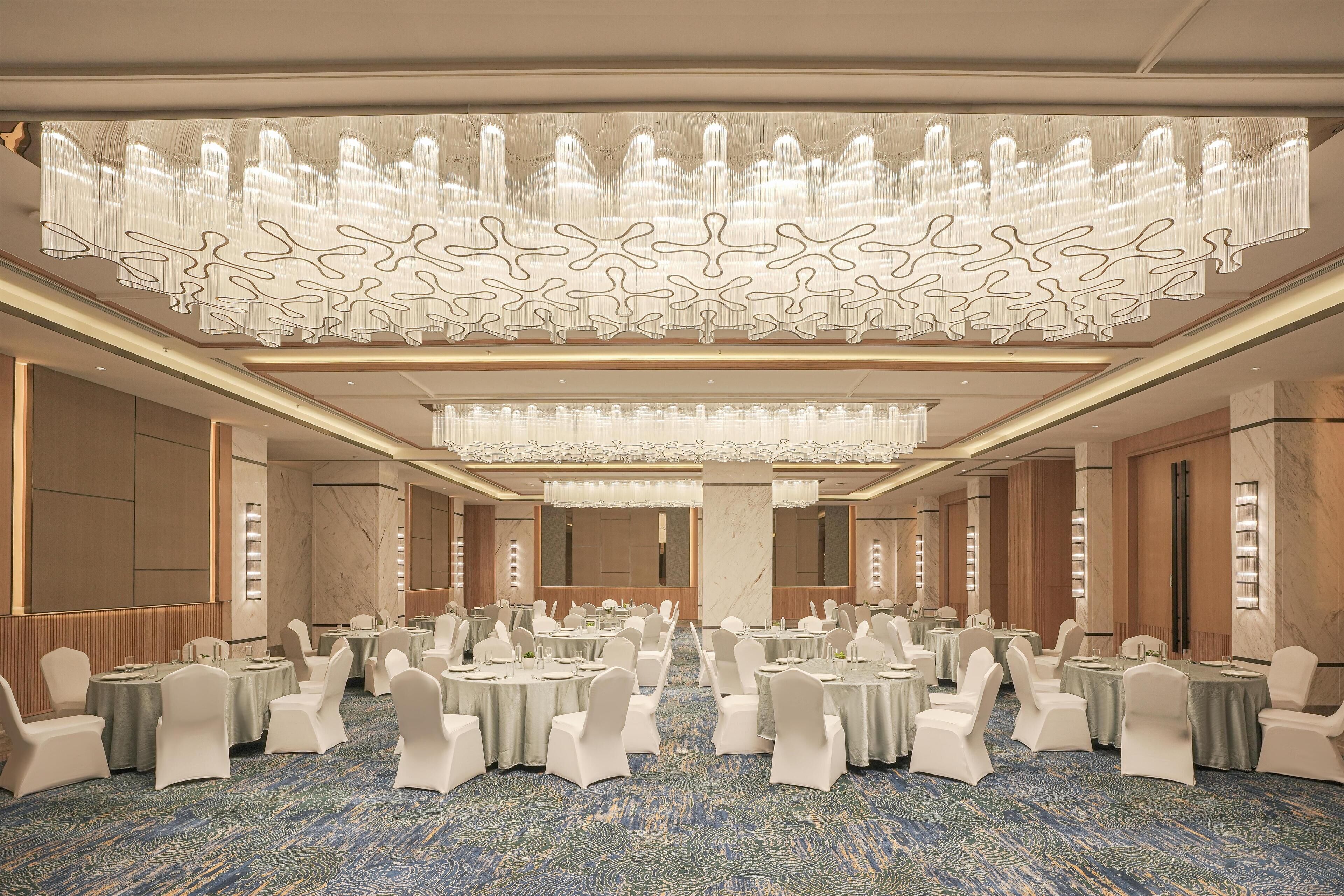 A banquet hall with round tables, white chairs, and a patterned carpet.