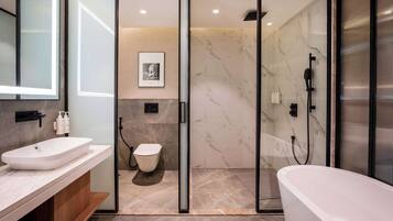 A modern bathroom with a white sink, toilet, and bathtub, marble walls, and a glass shower enclosure.
