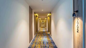 Un couloir d’hôtel avec un tapis à motifs, des portes en bois et un panneau indiquant le numéro de la chambre sur le mur.