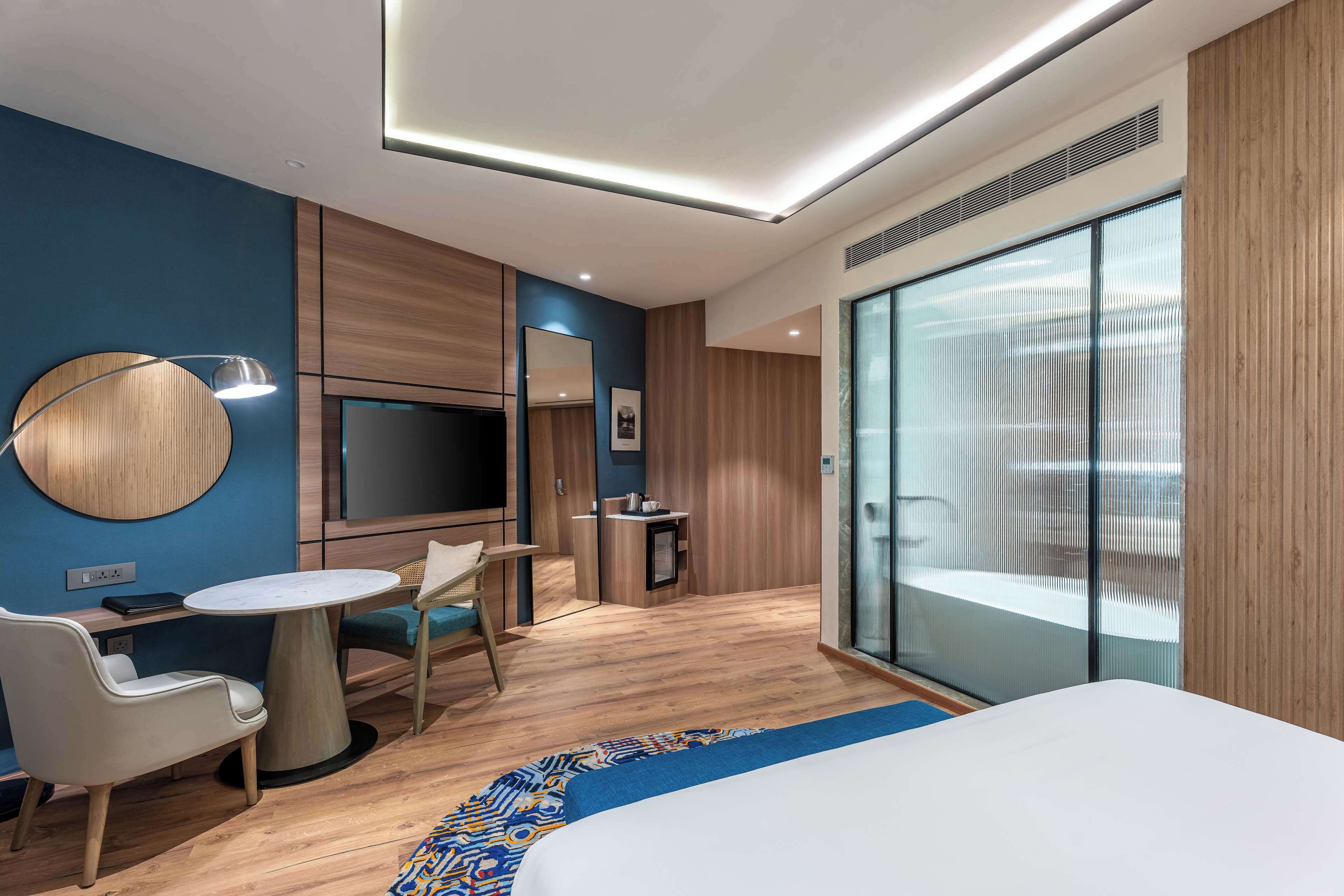 Een moderne hotelkamer met een bed, een bureau, een stoel, een televisie en een groot raam.