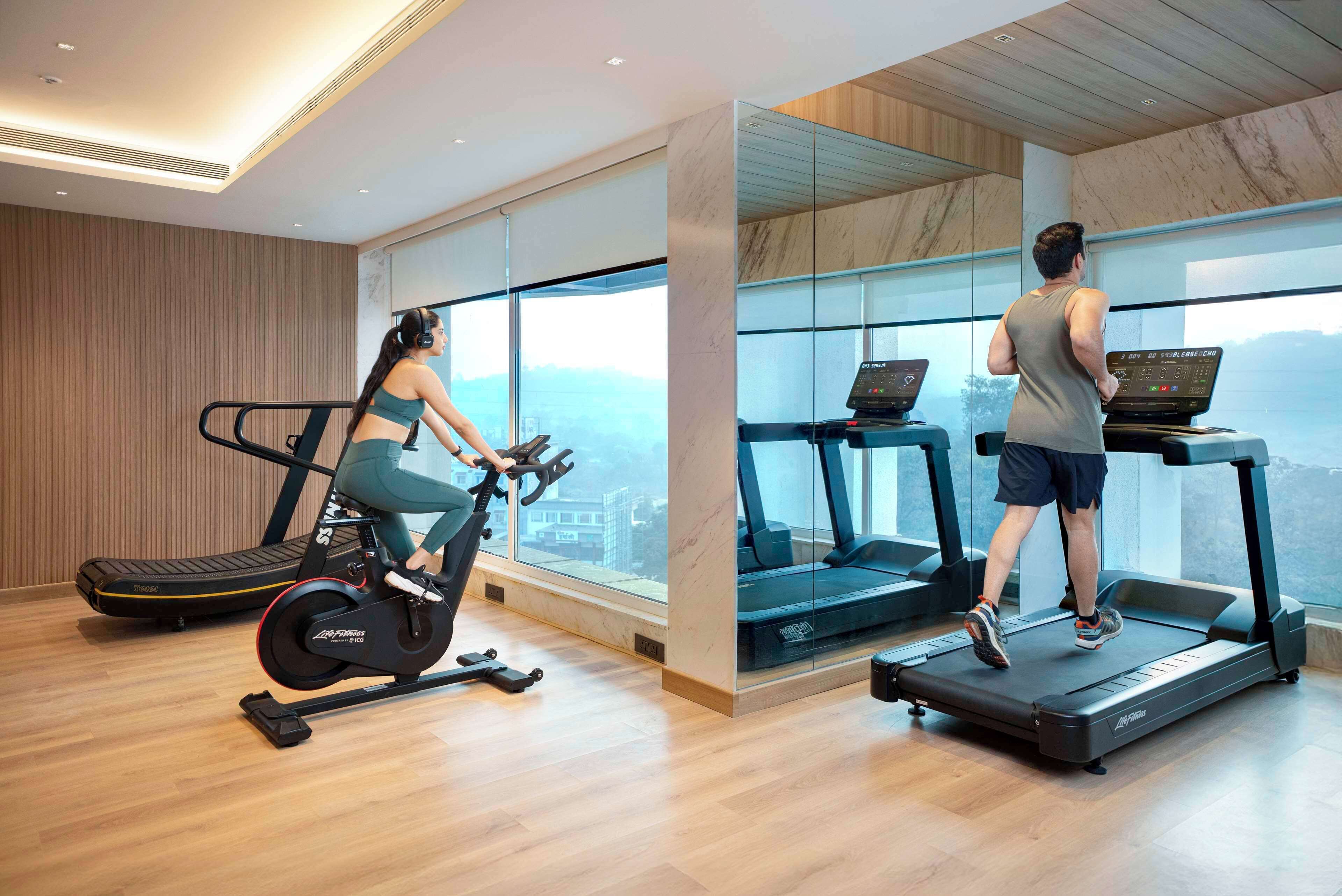 Een moderne sportschool met loopband, hometrainer en een groot raam met uitzicht op de stad.