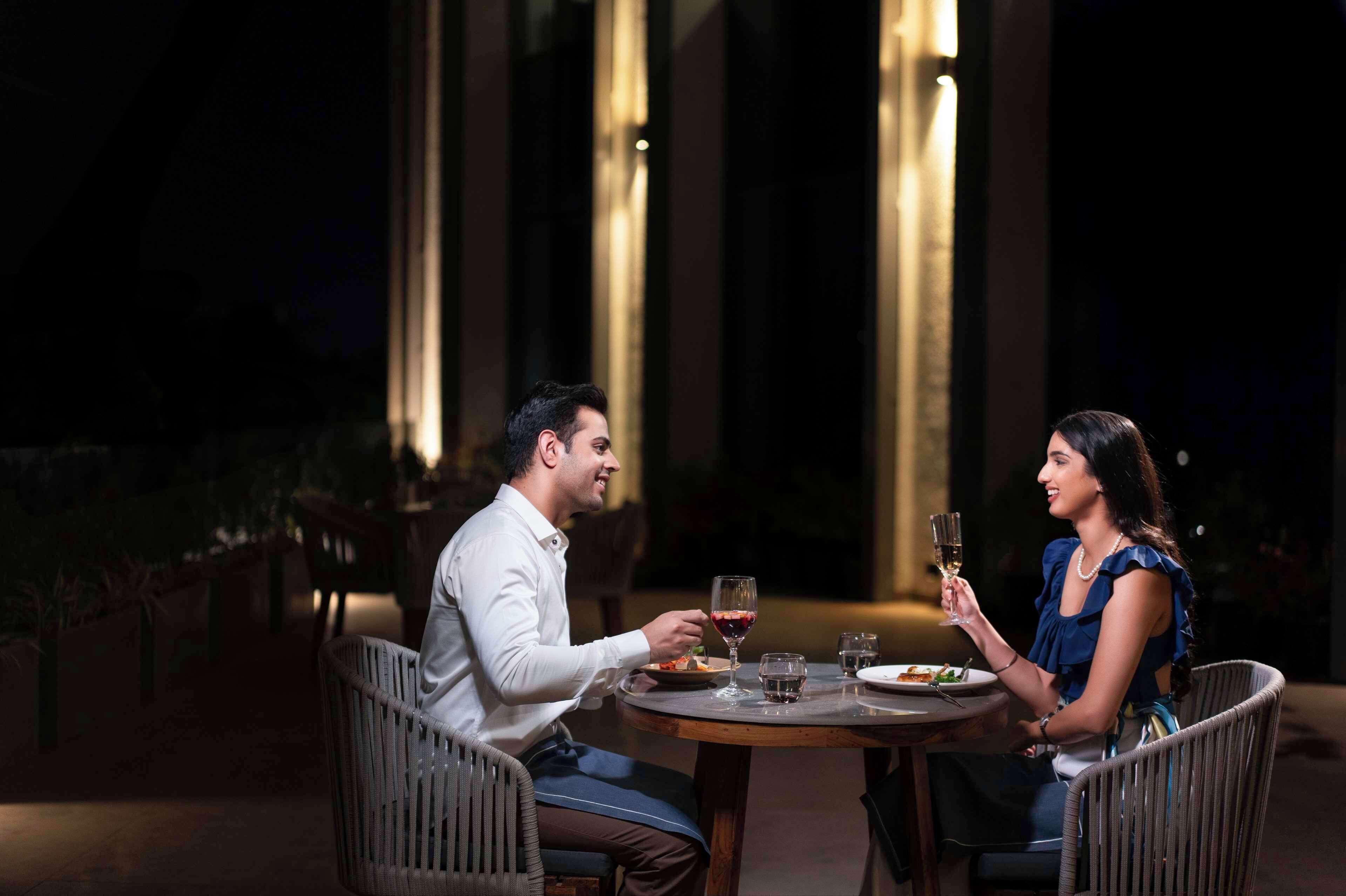 A couple dining at an outdoor table with a view of tall buildings in the background.