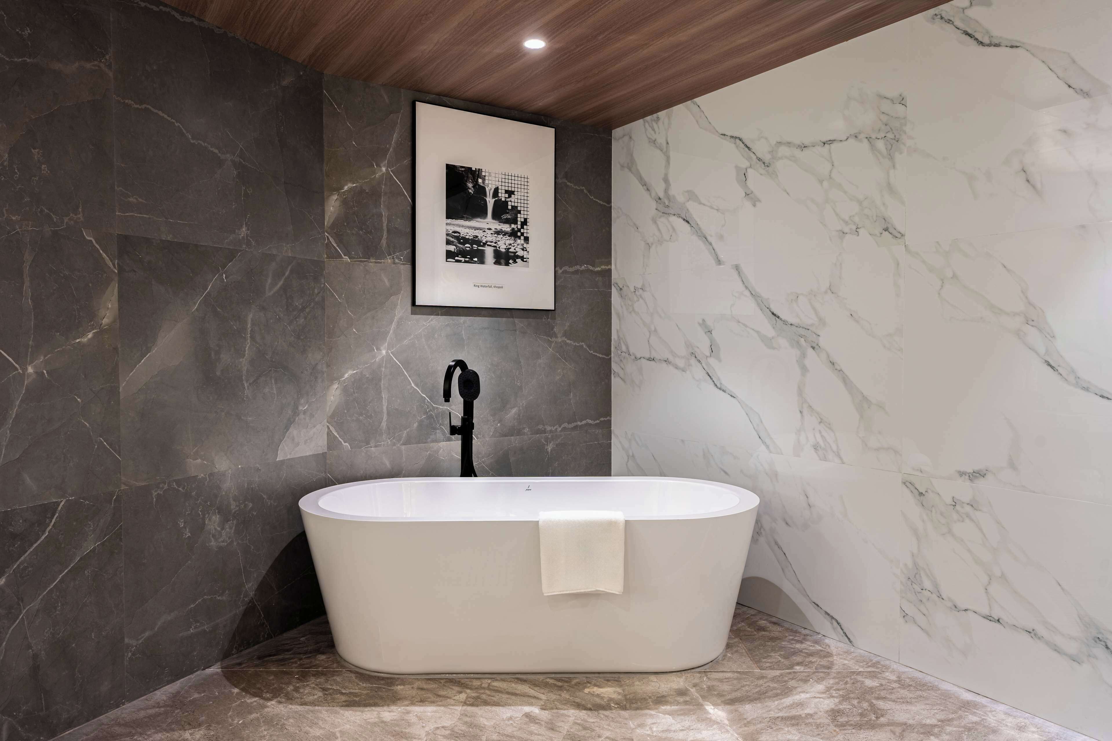 Un bagno moderno con una vasca freestanding, pareti in marmo scuro e un quadro appeso al muro.
