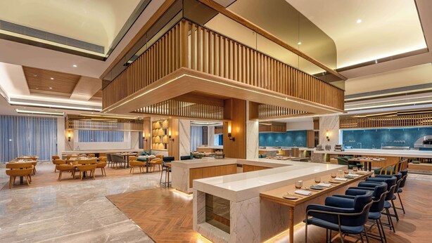 Un'ampia hall d'albergo con un'area bar centrale, zone salotto e un soffitto alto impreziosito da pannelli in legno.