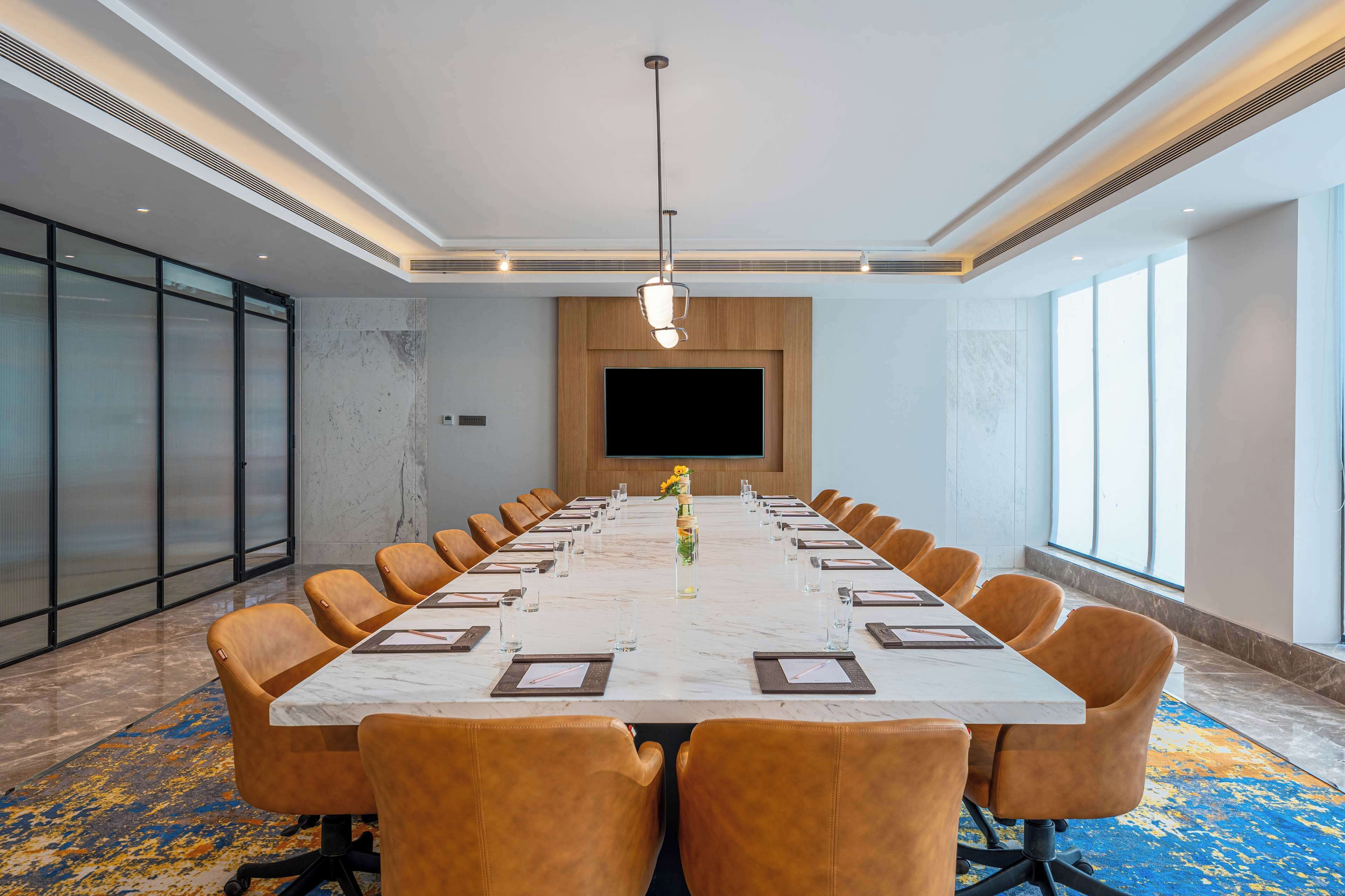 A conference room with a long table, comfortable chairs, a large screen, and a patterned carpet.