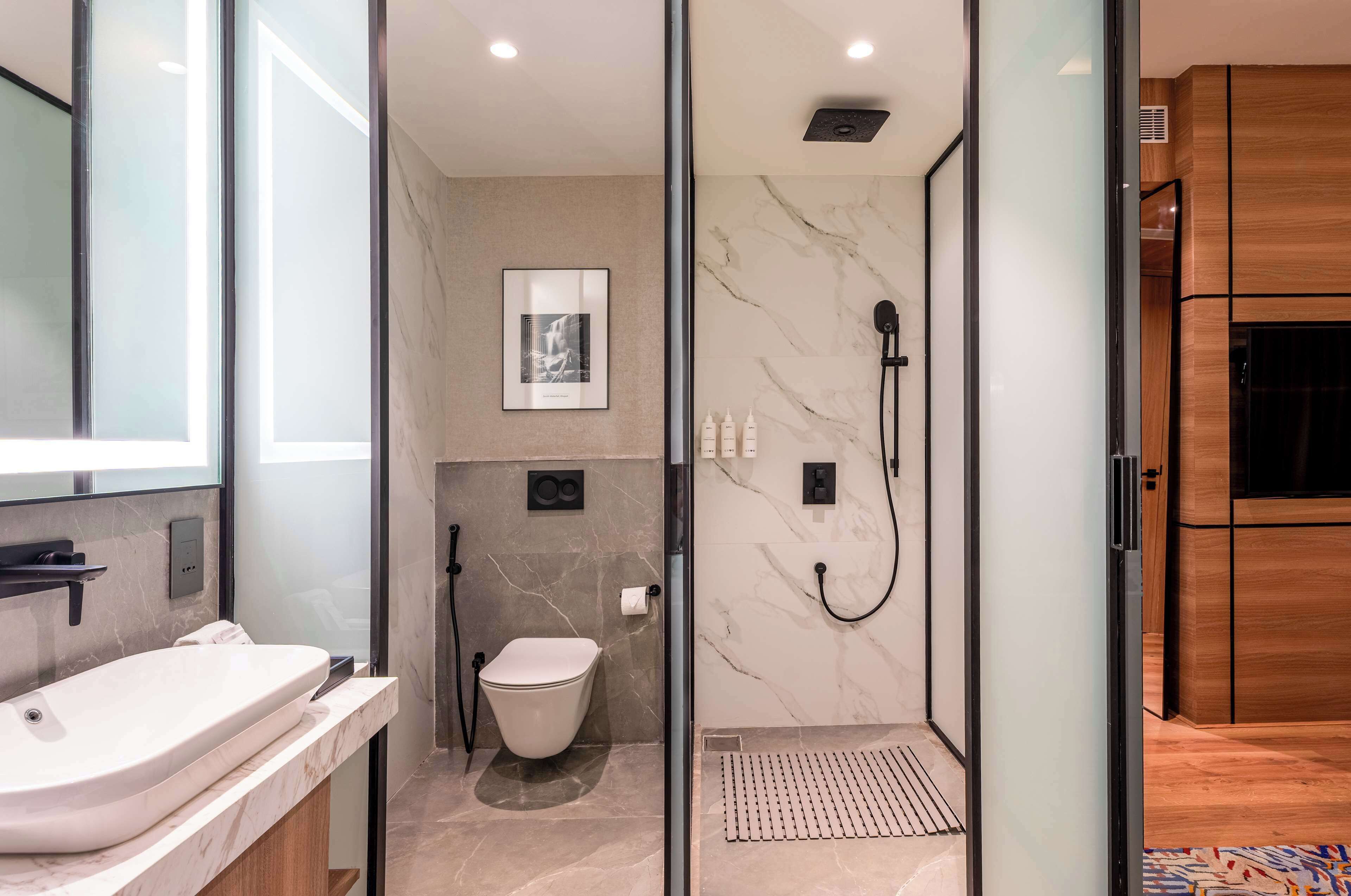 A modern bathroom with a glass-enclosed shower, a toilet, and a sink.