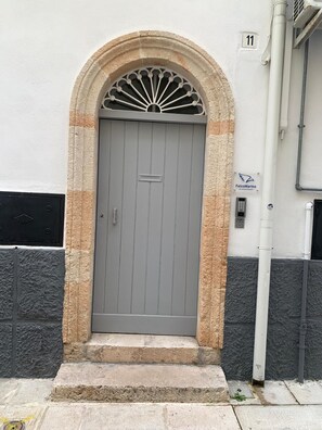 A grey door with a stone archway, a mailbox, and a number '11' sign on a white wall.