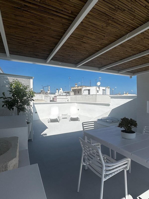 A rooftop terrace with a view of buildings, a table with chairs, and a potted plant.