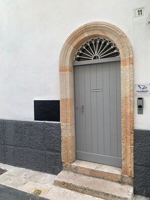 A grey door with a stone archway, a mailbox, and a number '11' sign on a white wall.