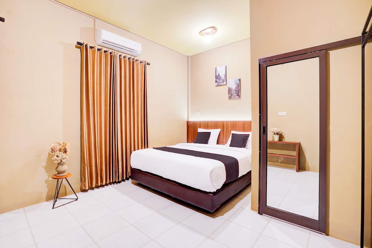Quarto de hotel com uma cama, um espelho, uma mesa pequena com um vaso e uma janela com cortinas.