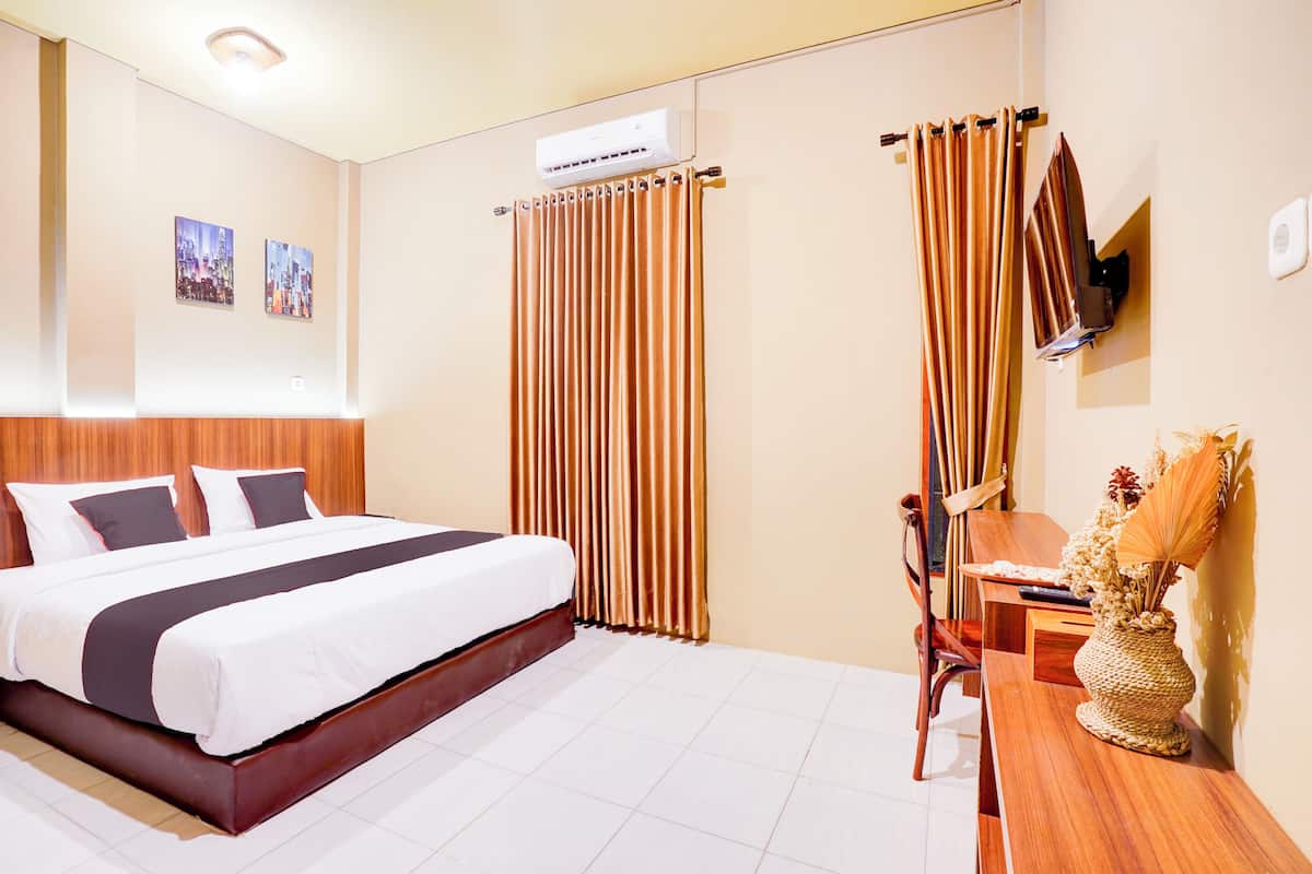 Quarto de hotel com uma cama grande, cabeceira de madeira, escrivaninha com cadeira e televisão na parede.