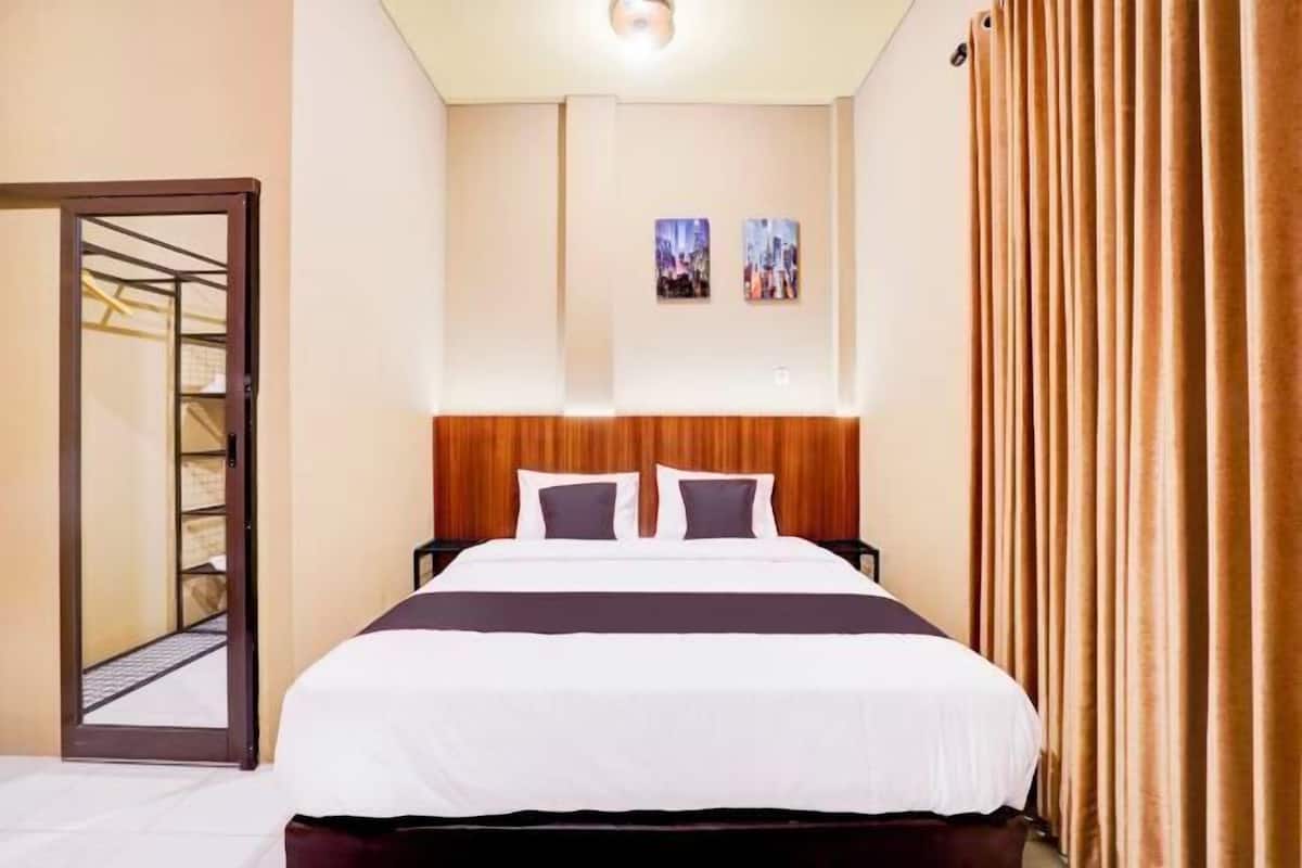 Quarto de hotel com cama, cabeceira de madeira, porta com espelho e duas imagens emolduradas na parede.