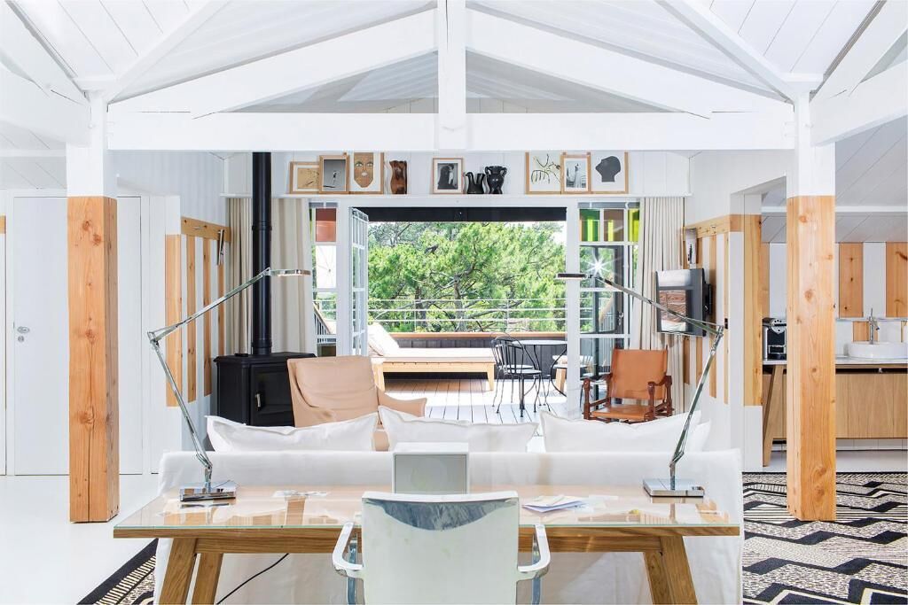 Een modern interieur met een glazen eettafel, witte banken en uitzicht op groen buiten.