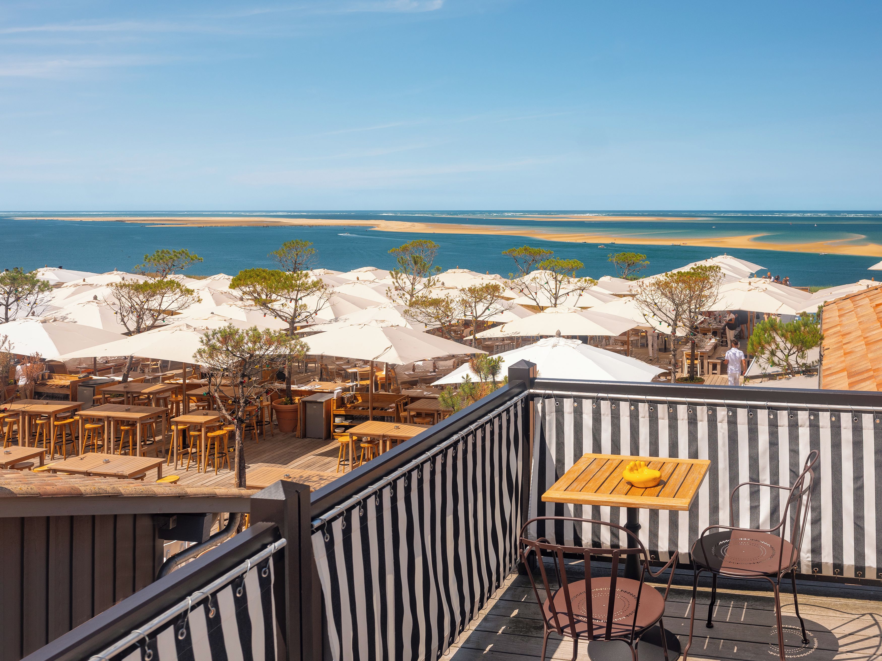 A terrace with outdoor seating overlooking a beach and the sea.