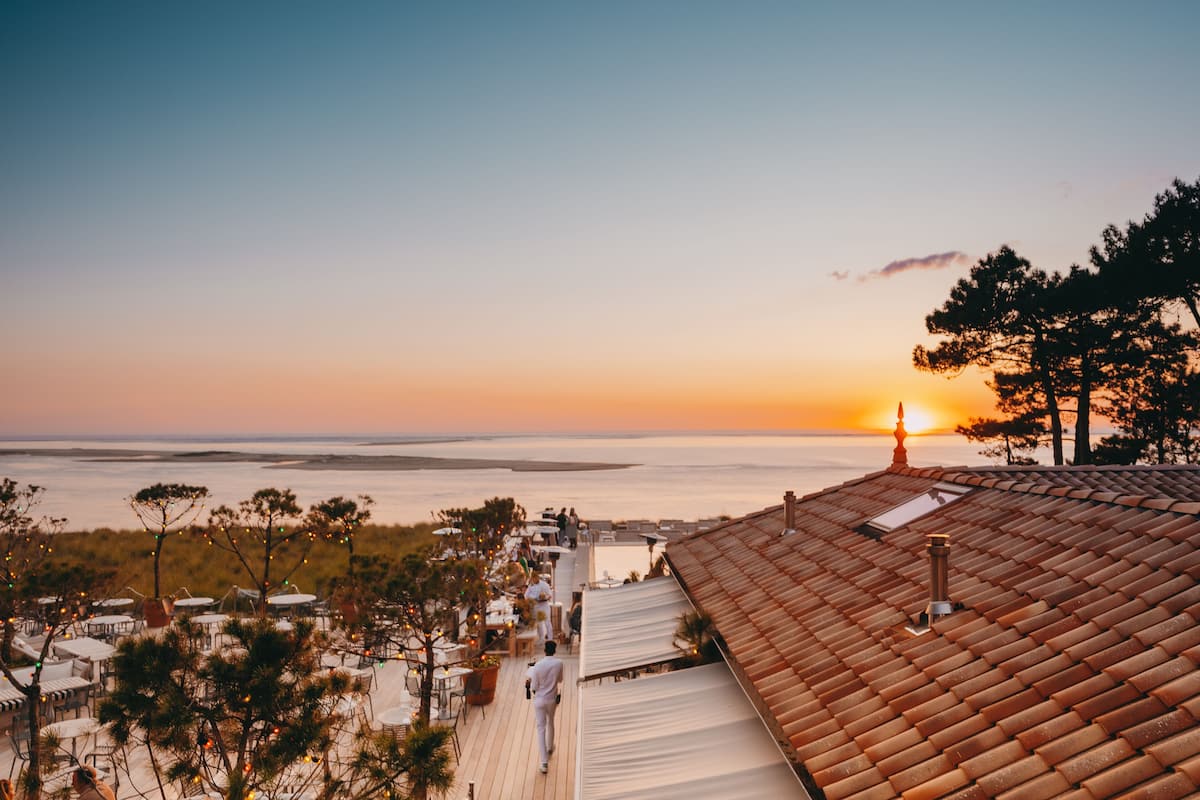 A rooftop terrace with outdoor seating and a view of the sunset over the water.
