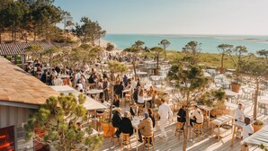 An outdoor dining area with tables and chairs, overlooking a beach and the sea. - La Co(o)rniche (La Teste-de-Buch)