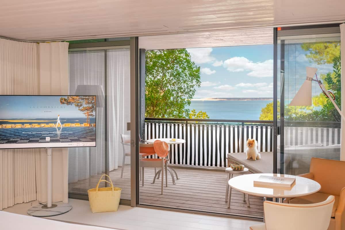 A modern hotel room with a balcony, a television, a dining area, and a view of the sea.