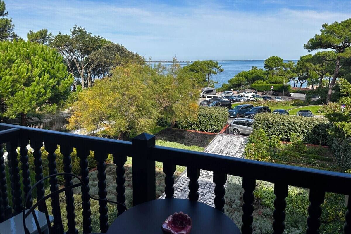 A balcony with a view of a parking area and trees, overlooking a body of water.