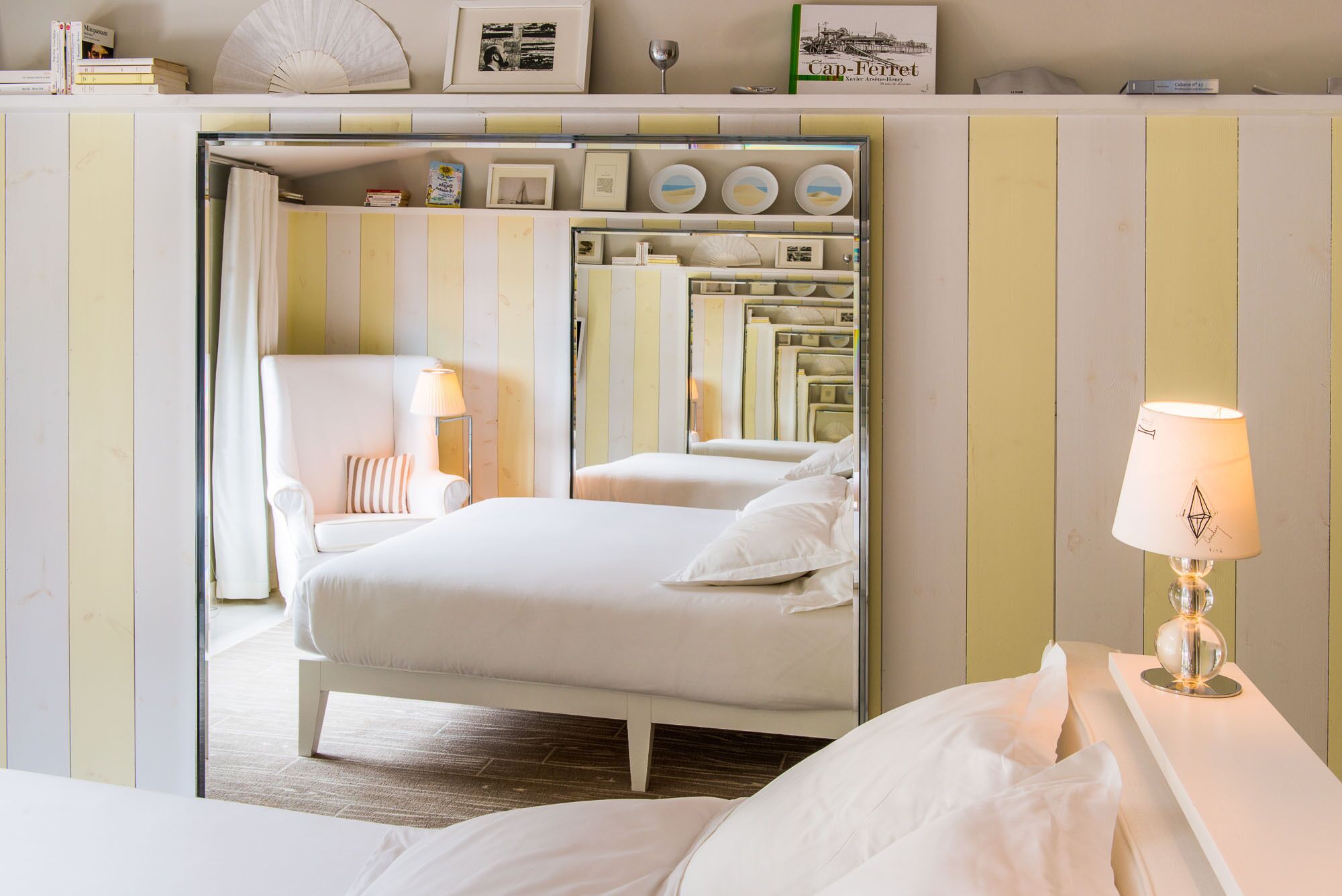 Une chambre d’hôtel comprenant un lit, une chaise, une lampe et une étagère avec des livres et des objets décoratifs.