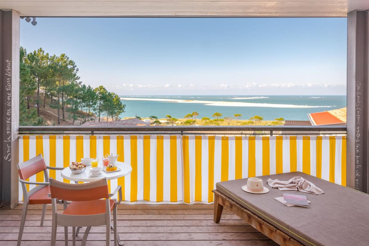 A balcony with a view of the sea, a table with breakfast, and a bed.