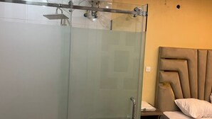 Un baño con cabina de ducha de vidrio, una cama con cabecero y una mesita de noche.