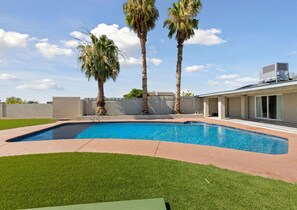 Una piscina rettangolare con bordo curvo, circondata da un prato ben curato e due palme.