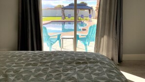 A room with a bed, a view of an outdoor pool area with chairs and a gazebo. - Luxury Vegas Getaway Pickleball, Pool & Game Room! (Las Vegas)