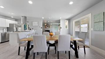 Een moderne keuken met witte kasten, een centraal eiland en een eethoek met een houten tafel en stoelen.