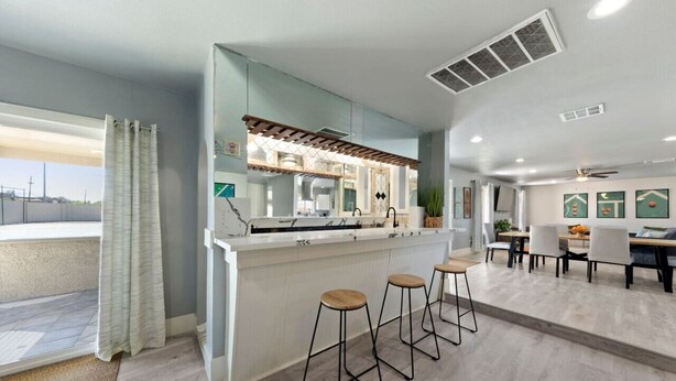 A modern kitchen with a marble countertop, bar stools, and a dining area with a table and chairs. - Luxury Vegas Getaway Pickleball, Pool & Game Room! (Las Vegas)