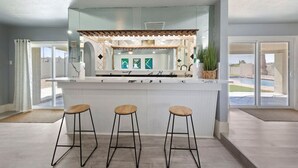 A kitchen with a central island, three stools, and a view of the outdoors. - Luxury Vegas Getaway Pickleball, Pool & Game Room! (Las Vegas)