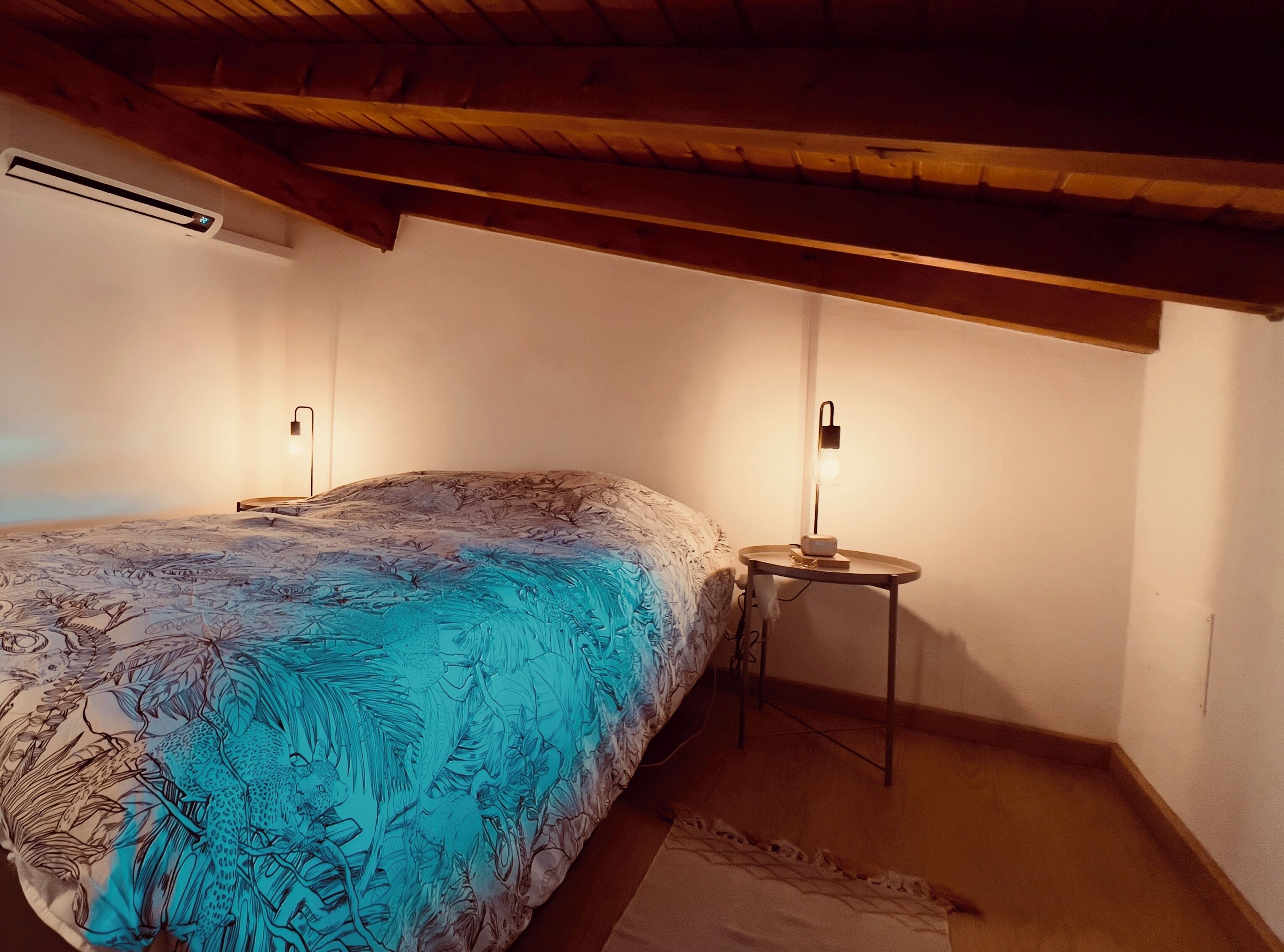 Un dormitorio con una cama, dos mesitas de noche, aire acondicionado instalado en la pared y techo de madera.